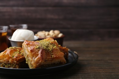 Photo of Delicious baklava with crushed nuts and ice cream on wooden table, closeup. Space for text