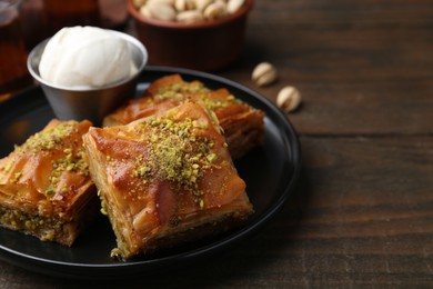 Delicious baklava with crushed nuts and ice cream on wooden table, closeup. Space for text