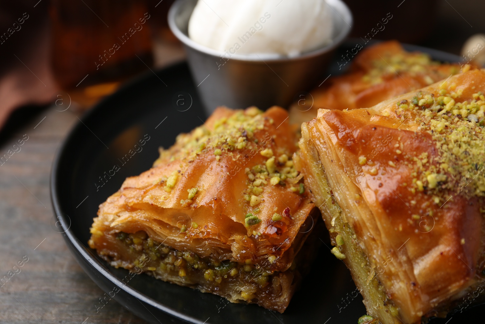 Photo of Delicious baklava with crushed nuts and ice cream on wooden table, closeup