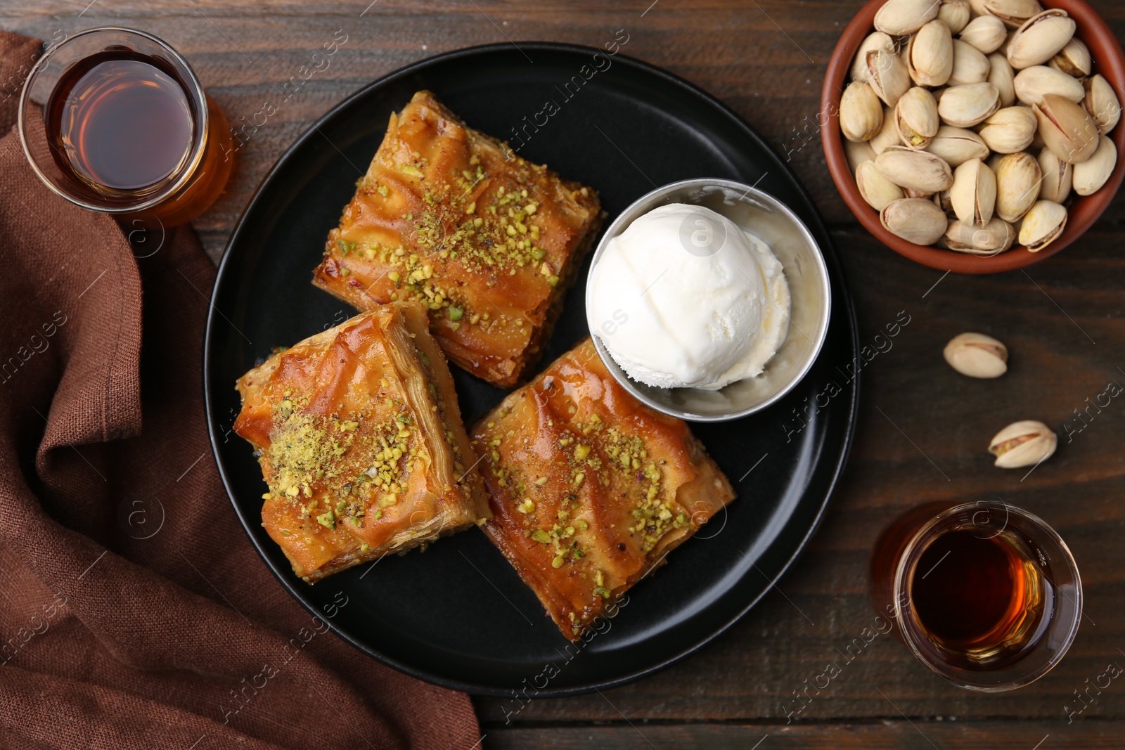 Photo of Delicious baklava with crushed nuts and ice cream served on wooden table, flat lay