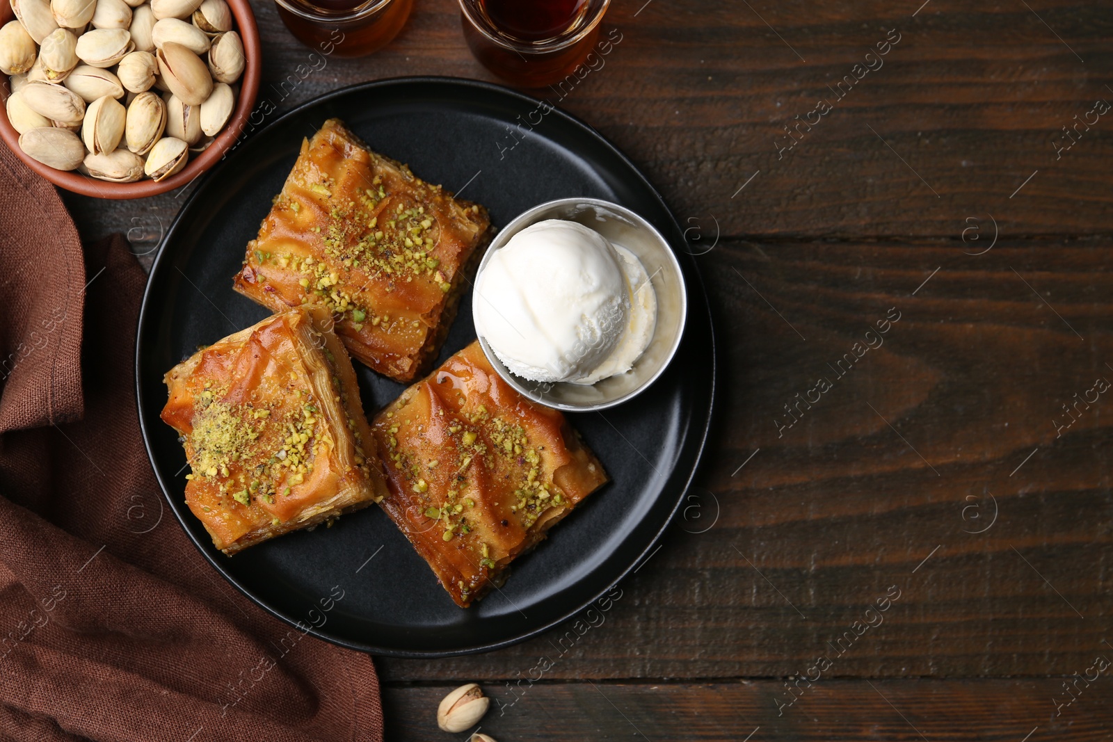 Photo of Delicious baklava with crushed nuts and ice cream on wooden table, flat lay. Space for text