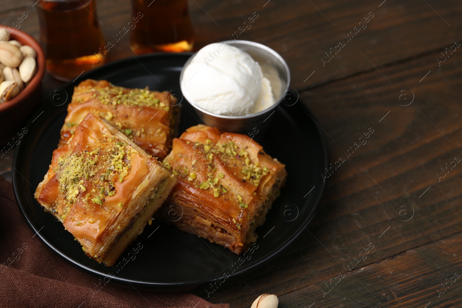 Photo of Delicious baklava with crushed nuts and ice cream served on wooden table, closeup. Space for text