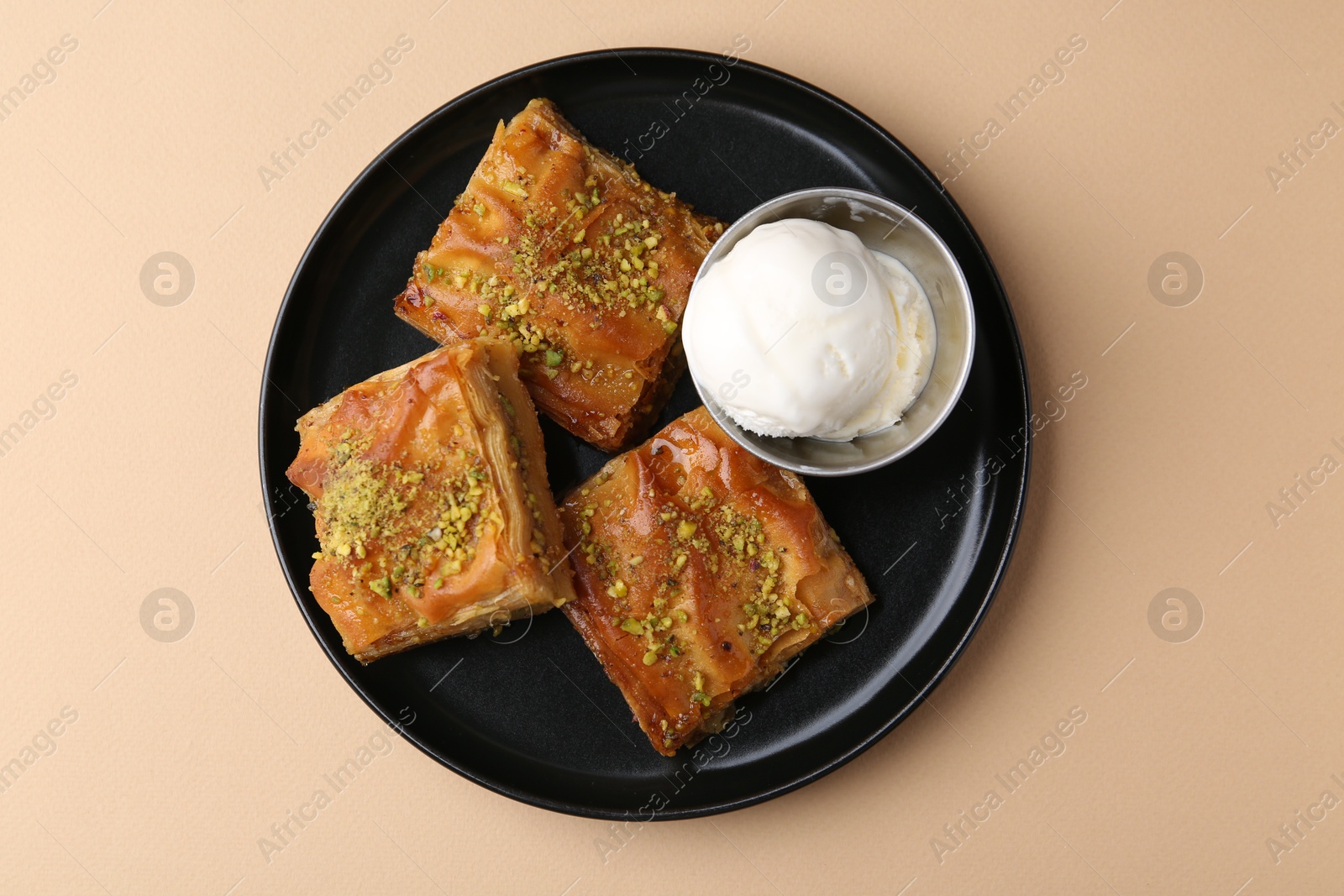 Photo of Delicious baklava with crushed nuts and ice cream on beige table, top view