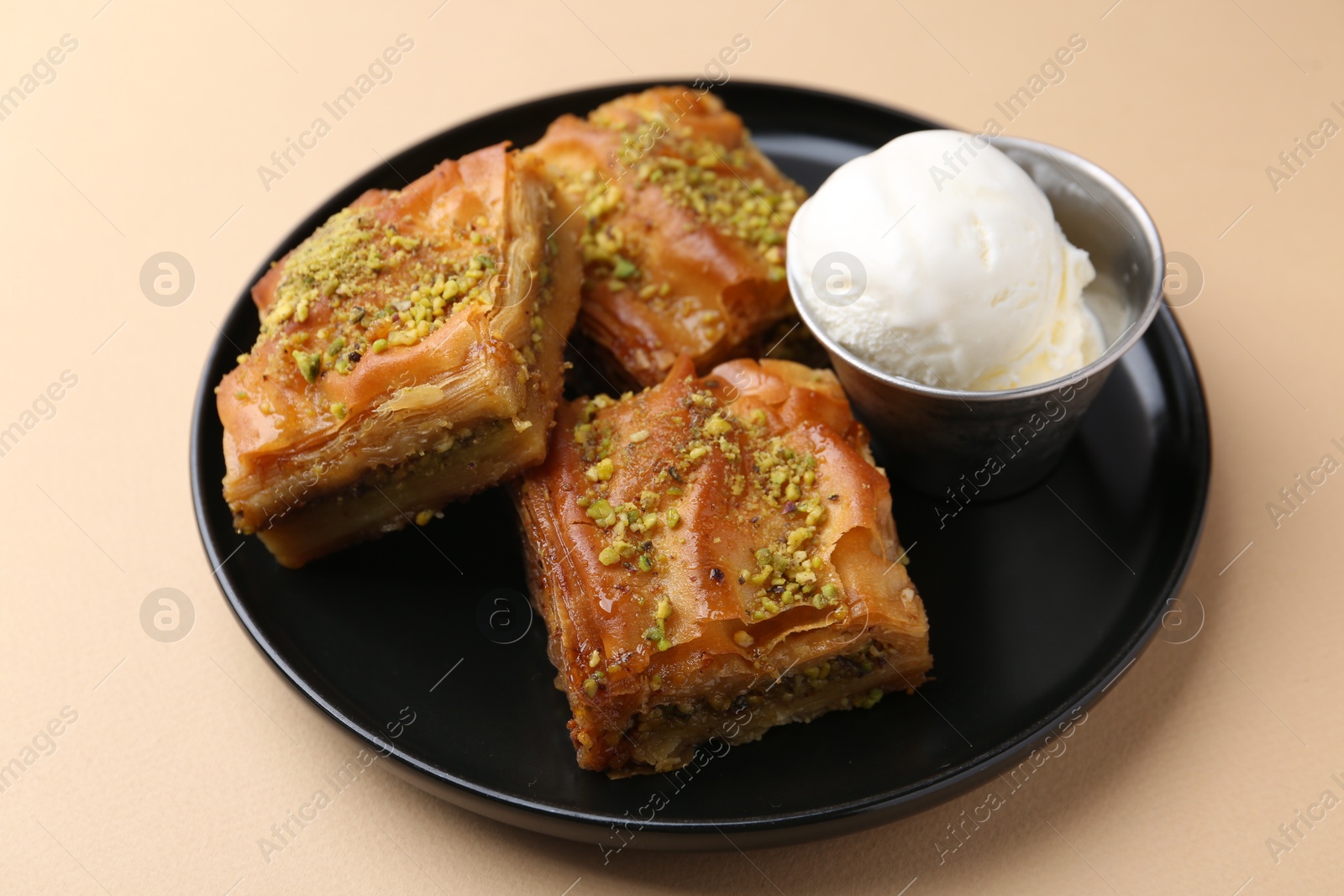 Photo of Delicious baklava with crushed nuts and ice cream on beige table, closeup