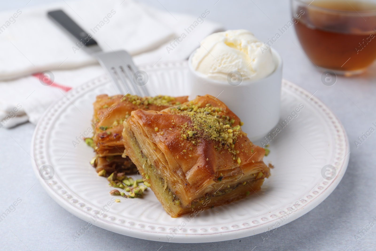 Photo of Delicious baklava with crushed nuts and ice cream on grey table, closeup