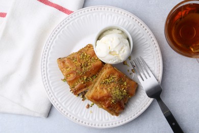 Photo of Delicious baklava with crushed nuts and ice cream served on grey table, flat lay