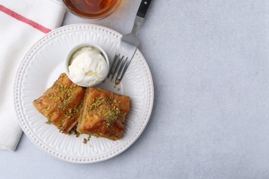 Photo of Delicious baklava with crushed nuts and ice cream served on grey table, flat lay. Space for text