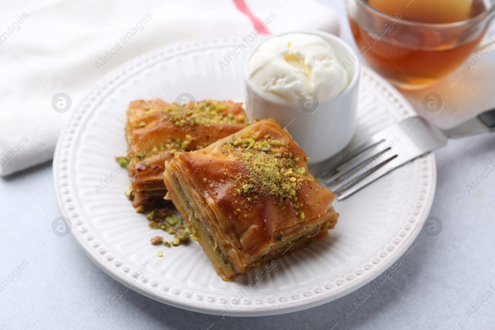 Photo of Delicious baklava with crushed nuts and ice cream on grey table, closeup
