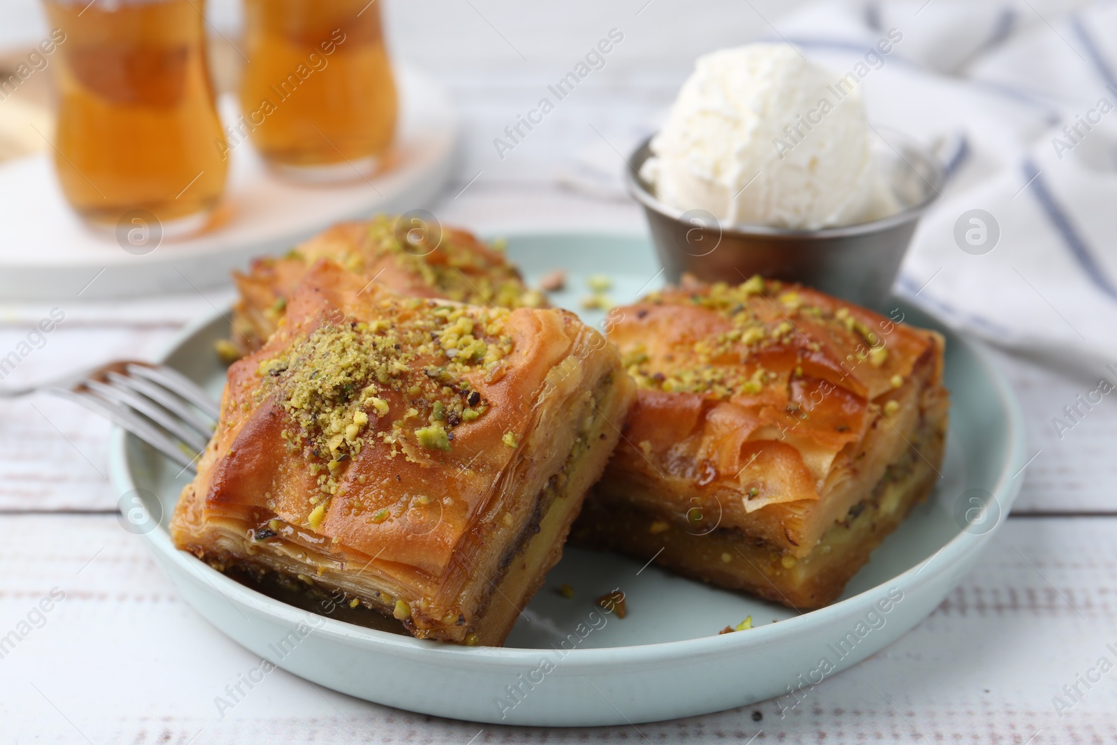 Photo of Delicious baklava with crushed nuts and ice cream on white wooden table, closeup