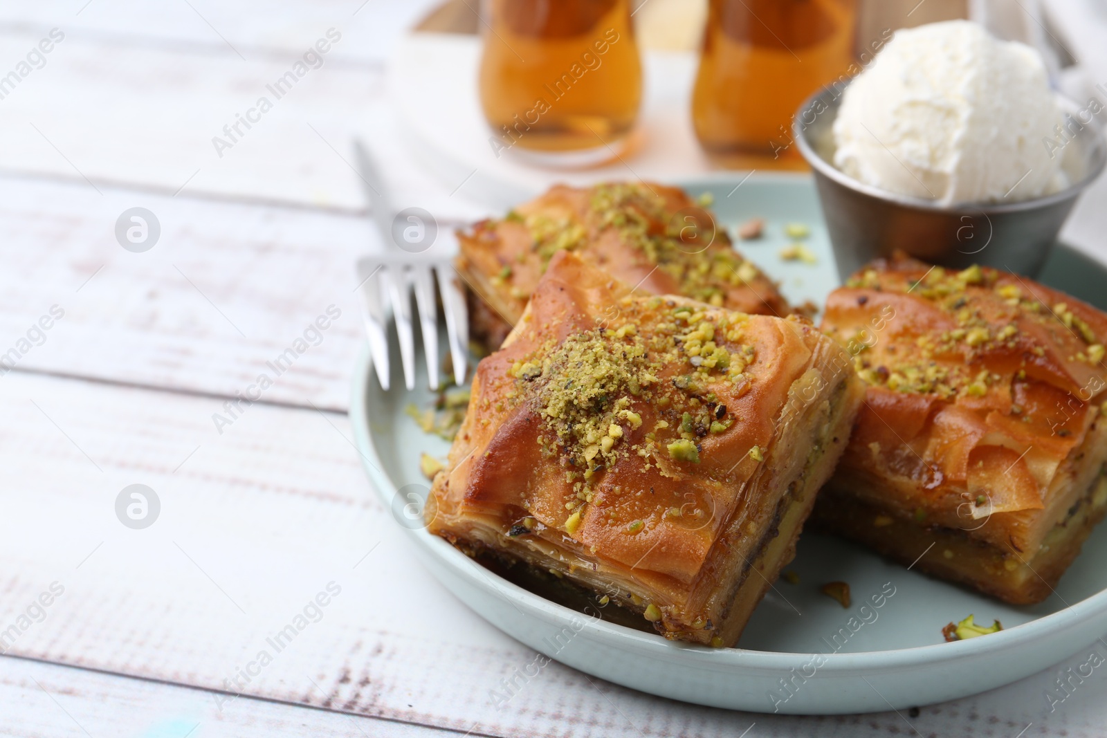 Photo of Delicious baklava with crushed nuts and ice cream on white wooden table, closeup. Space for text