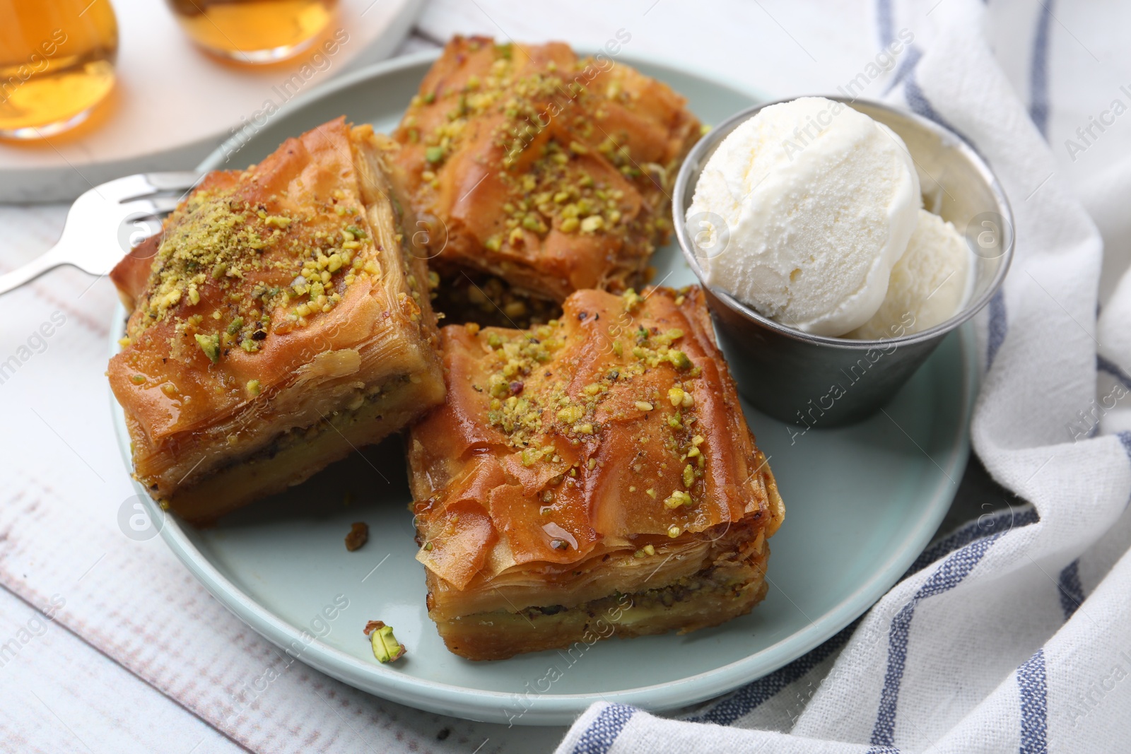 Photo of Delicious baklava with crushed nuts and ice cream on light wooden table, closeup