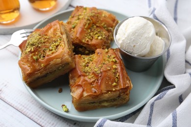 Photo of Delicious baklava with crushed nuts and ice cream on light wooden table, closeup