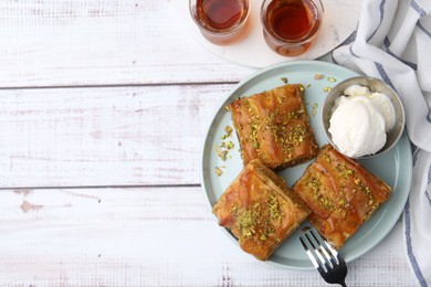 Photo of Delicious baklava with crushed nuts and ice cream served on light wooden table, flat lay. Space for text