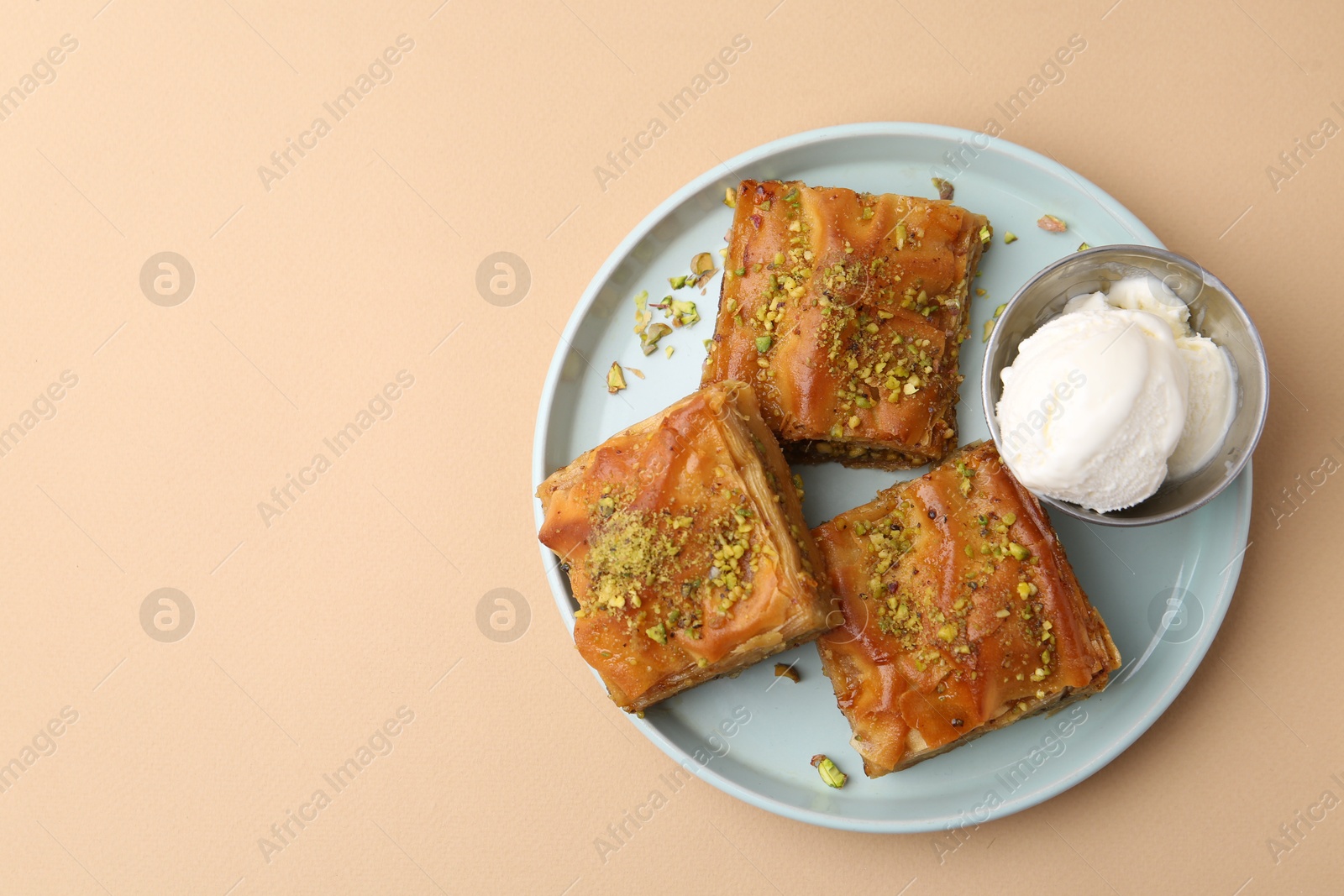 Photo of Delicious baklava with crushed nuts and ice cream on beige table, top view. Space for text