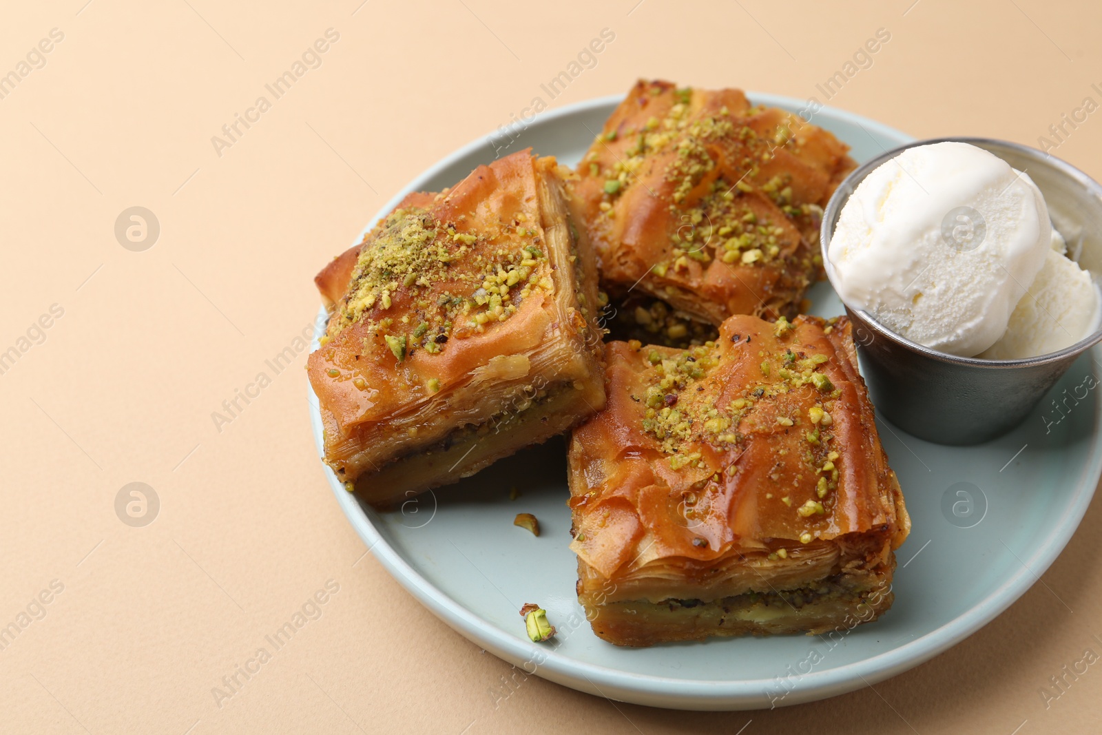 Photo of Delicious baklava with crushed nuts and ice cream on beige table, closeup. Space for text