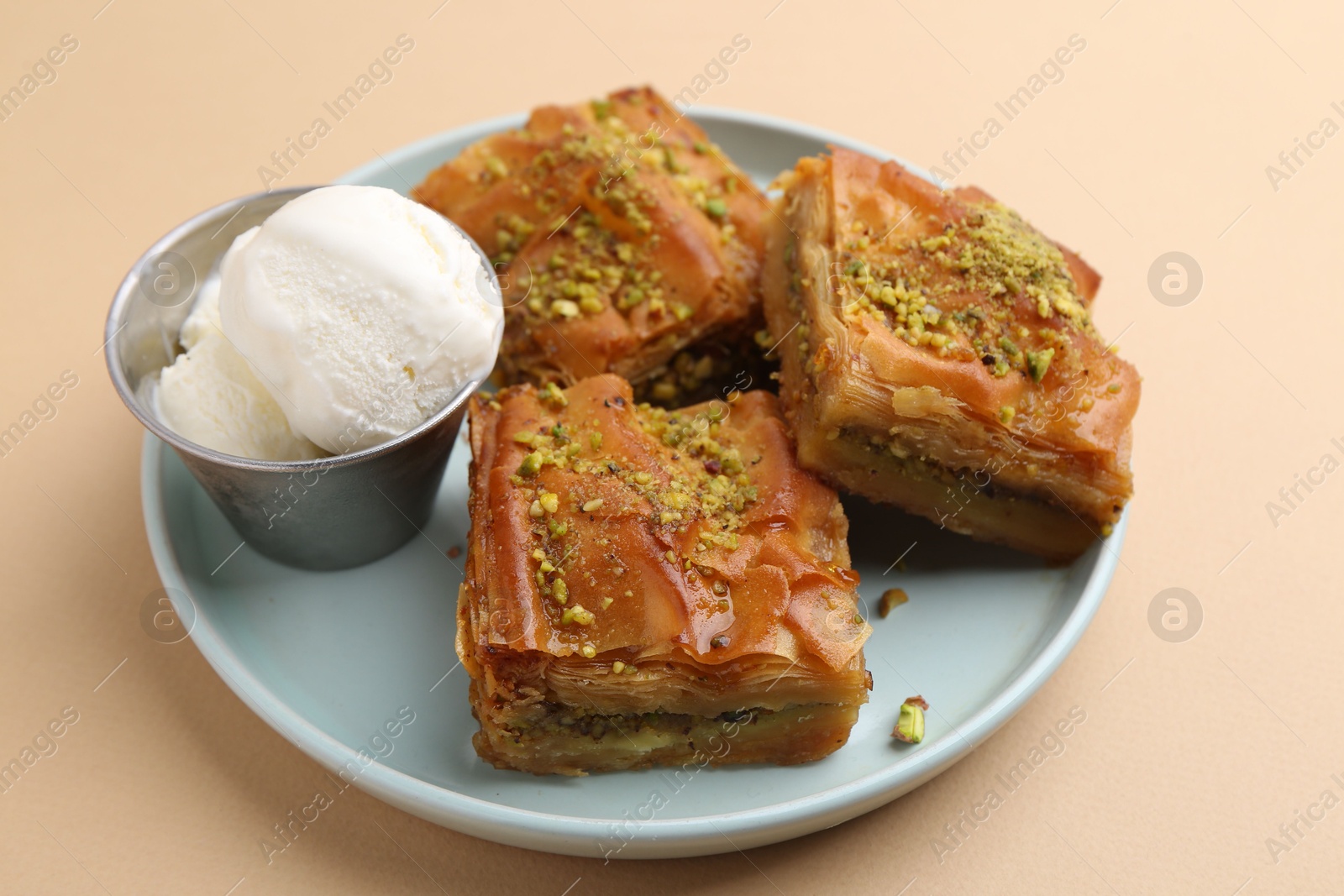 Photo of Delicious baklava with crushed nuts and ice cream on beige table, closeup