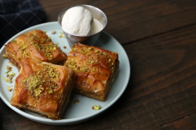 Photo of Delicious baklava with crushed nuts and ice cream on wooden table, closeup. Space for text