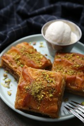 Photo of Delicious baklava with crushed nuts and ice cream on wooden table, closeup