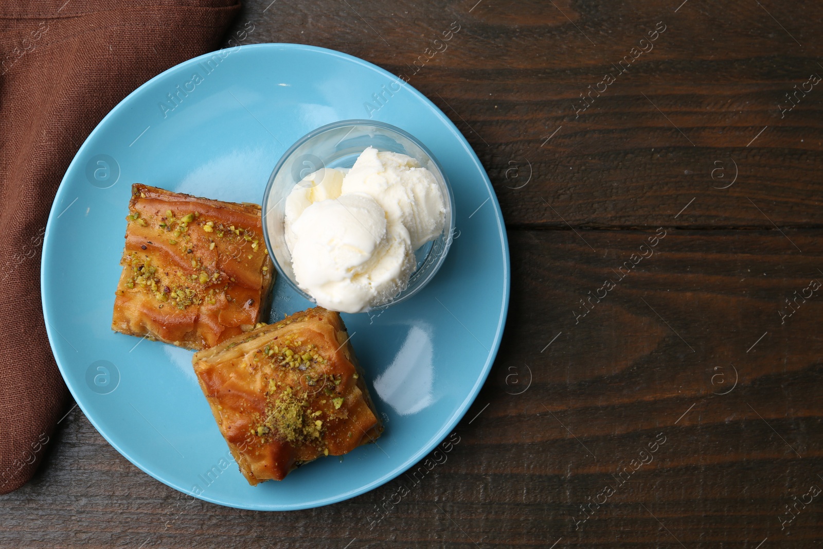Photo of Tasty baklava with chopped nuts and scoops of ice cream on wooden table, top view. Space for text