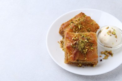 Photo of Tasty baklava with chopped nuts and scoop of ice cream on light grey table, closeup. Space for text