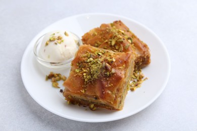 Tasty baklava with chopped nuts and scoop of ice cream on light grey table, closeup