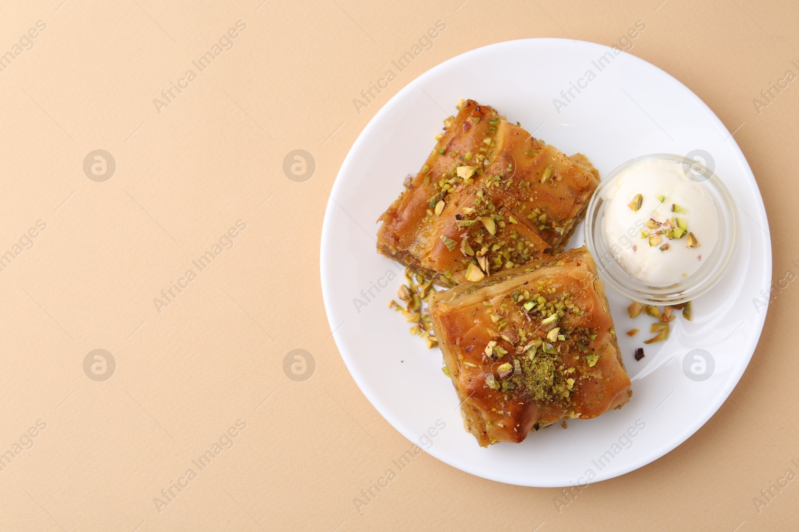 Photo of Tasty baklava with chopped nuts and scoop of ice cream on beige table, top view. Space for text