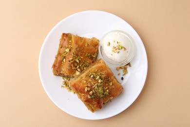 Photo of Tasty baklava with chopped nuts and scoop of ice cream on beige table, top view