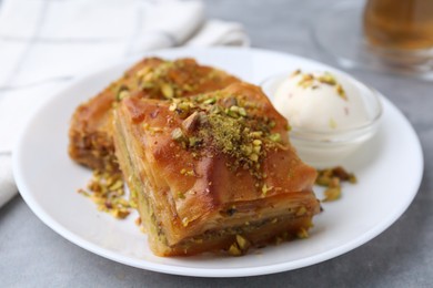 Photo of Tasty baklava with chopped nuts and scoop of ice cream on grey table, closeup