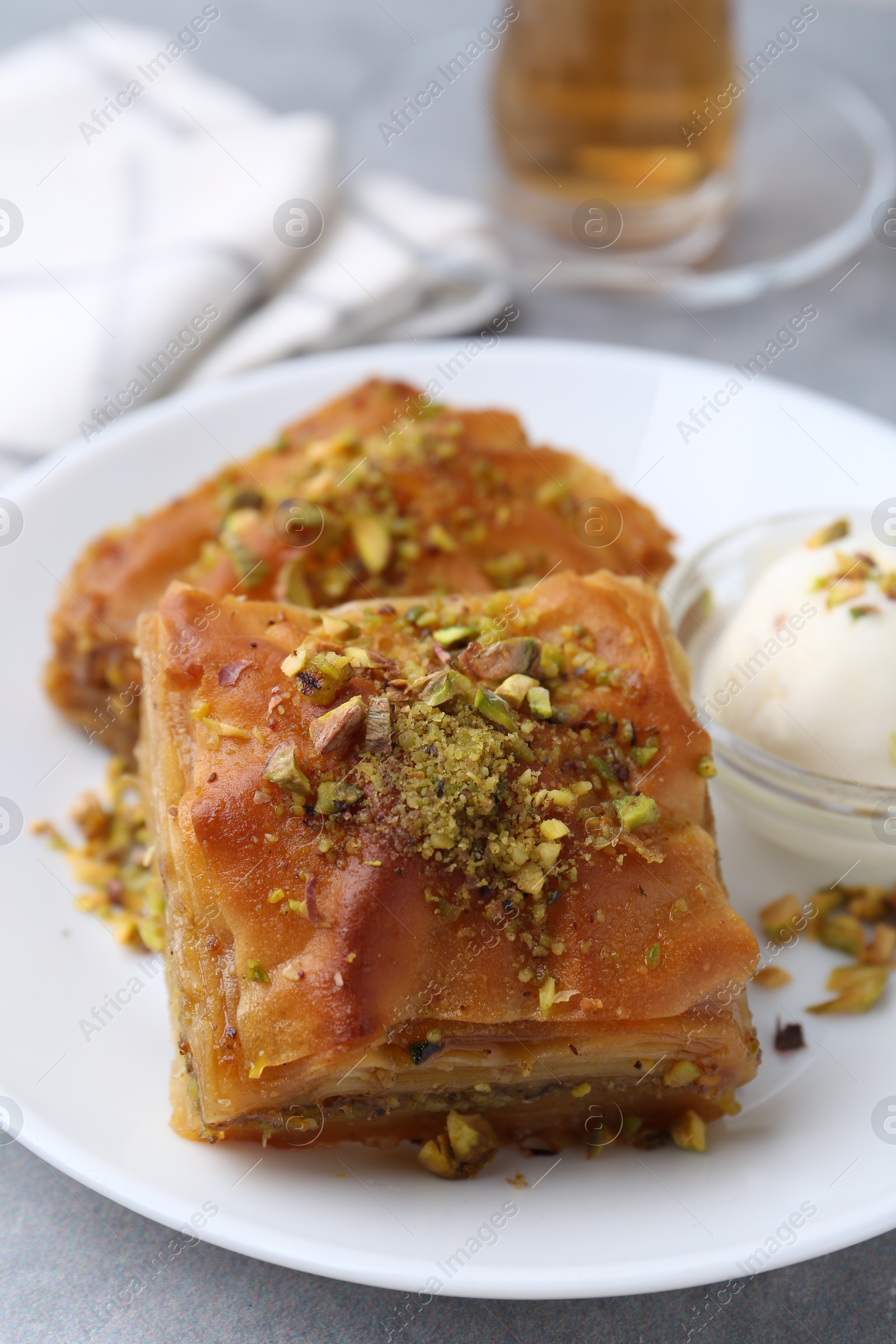 Photo of Tasty baklava with chopped nuts and scoop of ice cream on grey table, closeup