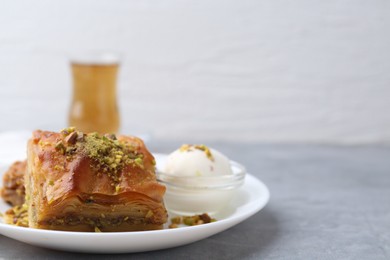 Photo of Tasty baklava with chopped nuts and scoop of ice cream on grey table, closeup. Space for text