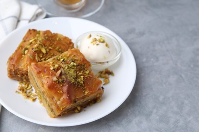 Photo of Tasty baklava with chopped nuts and scoop of ice cream on grey table, closeup. Space for text