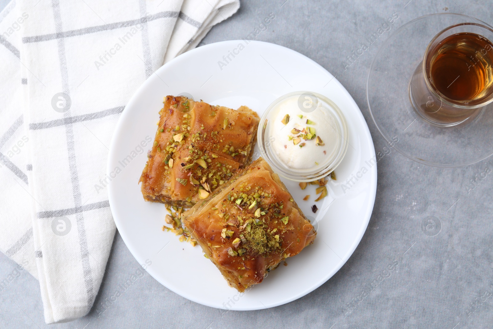 Photo of Tasty baklava with chopped nuts, scoop of ice cream and tea on grey table, top view