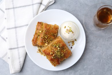 Photo of Tasty baklava with chopped nuts, scoop of ice cream and tea on grey table, top view