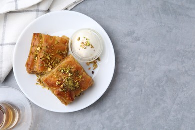 Photo of Tasty baklava with chopped nuts and scoop of ice cream on grey table, top view. Space for text