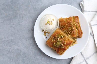 Photo of Tasty baklava with chopped nuts and scoop of ice cream on grey table, top view. Space for text