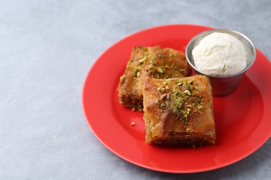 Photo of Tasty baklava with chopped nuts and scoop of ice cream on grey table, closeup. Space for text