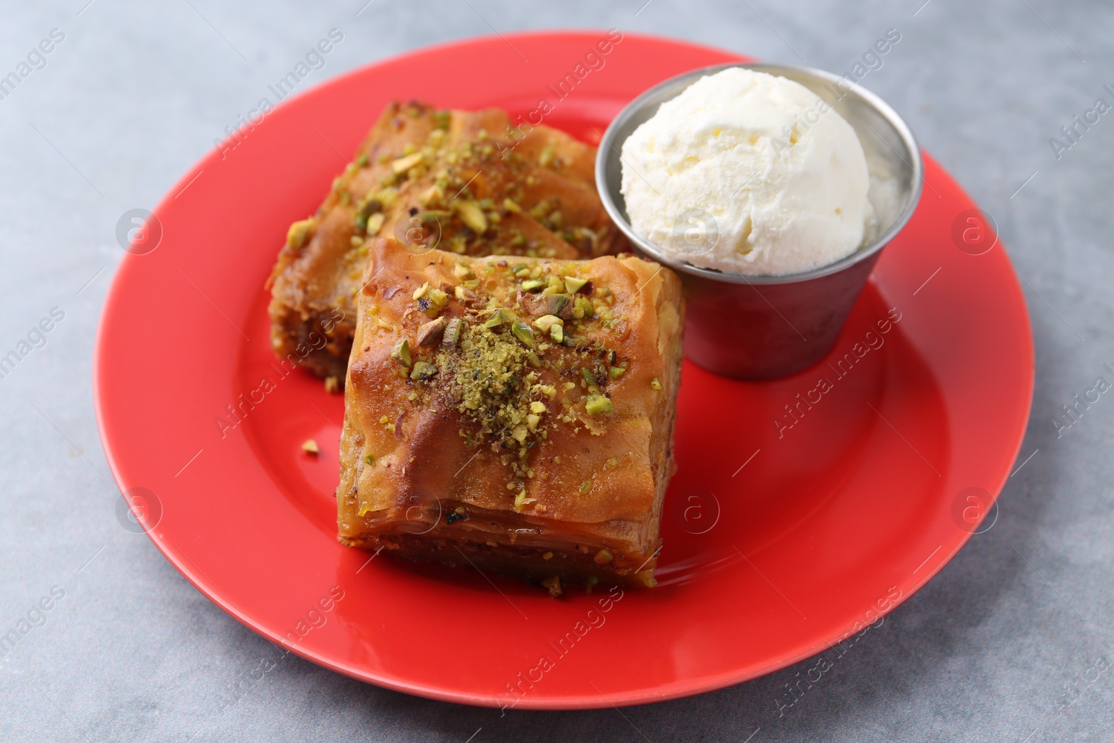 Photo of Tasty baklava with chopped nuts and scoop of ice cream on grey table, closeup