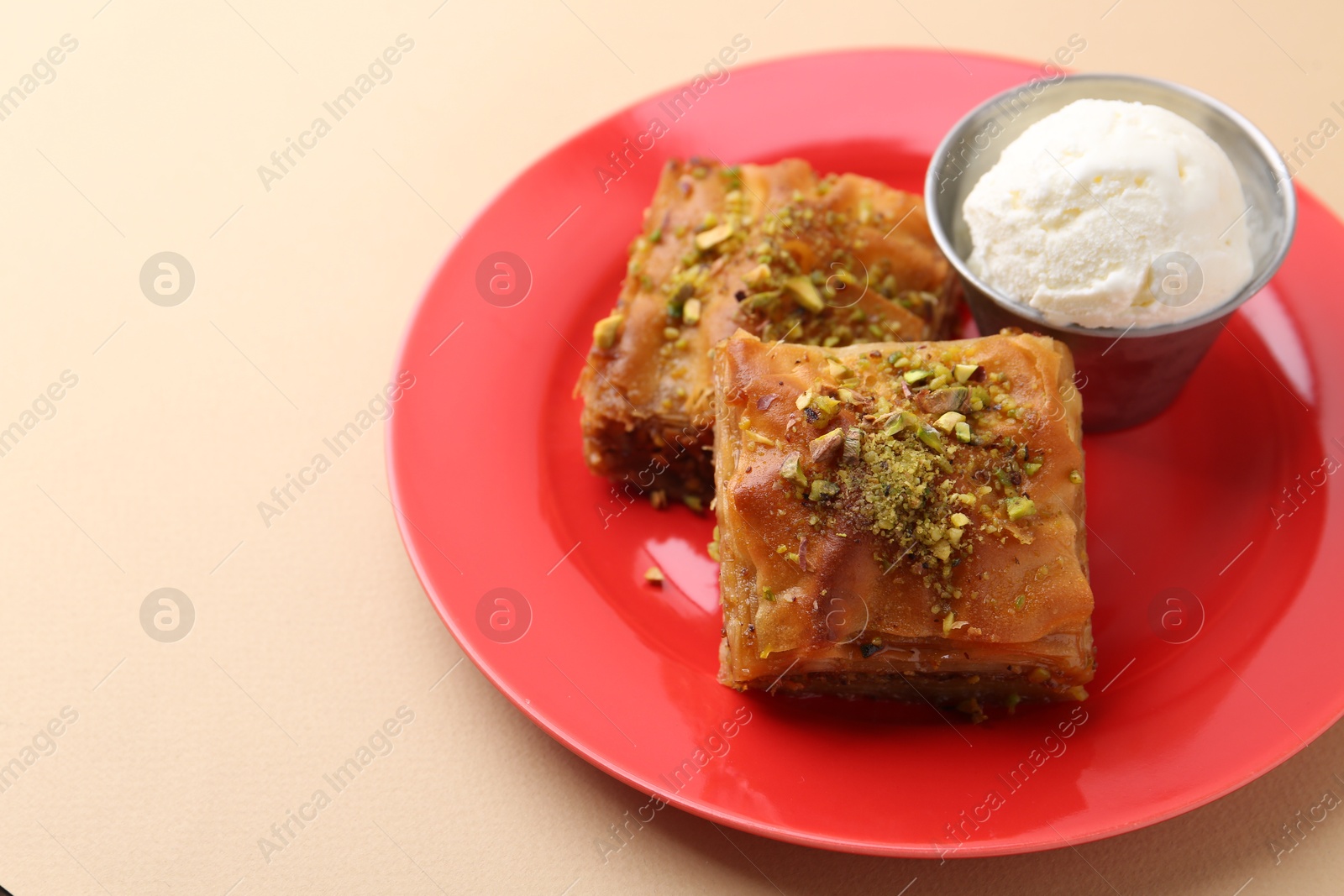 Photo of Tasty baklava with chopped nuts and scoop of ice cream on beige table, closeup. Space for text