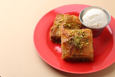 Photo of Tasty baklava with chopped nuts and scoop of ice cream on beige table, closeup. Space for text