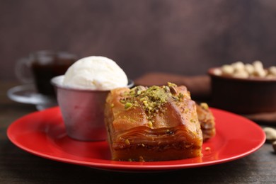 Photo of Tasty baklava with chopped nuts and scoop of ice cream on wooden table, closeup