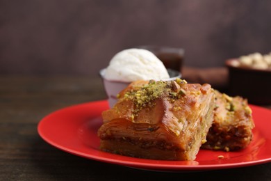 Photo of Tasty baklava with chopped nuts and scoop of ice cream on wooden table, closeup