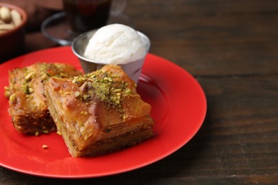 Photo of Tasty baklava with chopped nuts and scoop of ice cream on wooden table, closeup