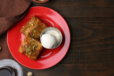 Photo of Tasty baklava with chopped nuts, scoop of ice cream and tea on wooden table, top view. Space for text