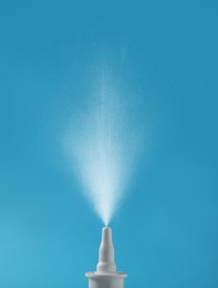 Image of Nasal spray with sprinkled medication over nozzle on light blue background, closeup