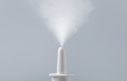 Image of Nasal spray with sprinkled medication over nozzle on grey background, closeup