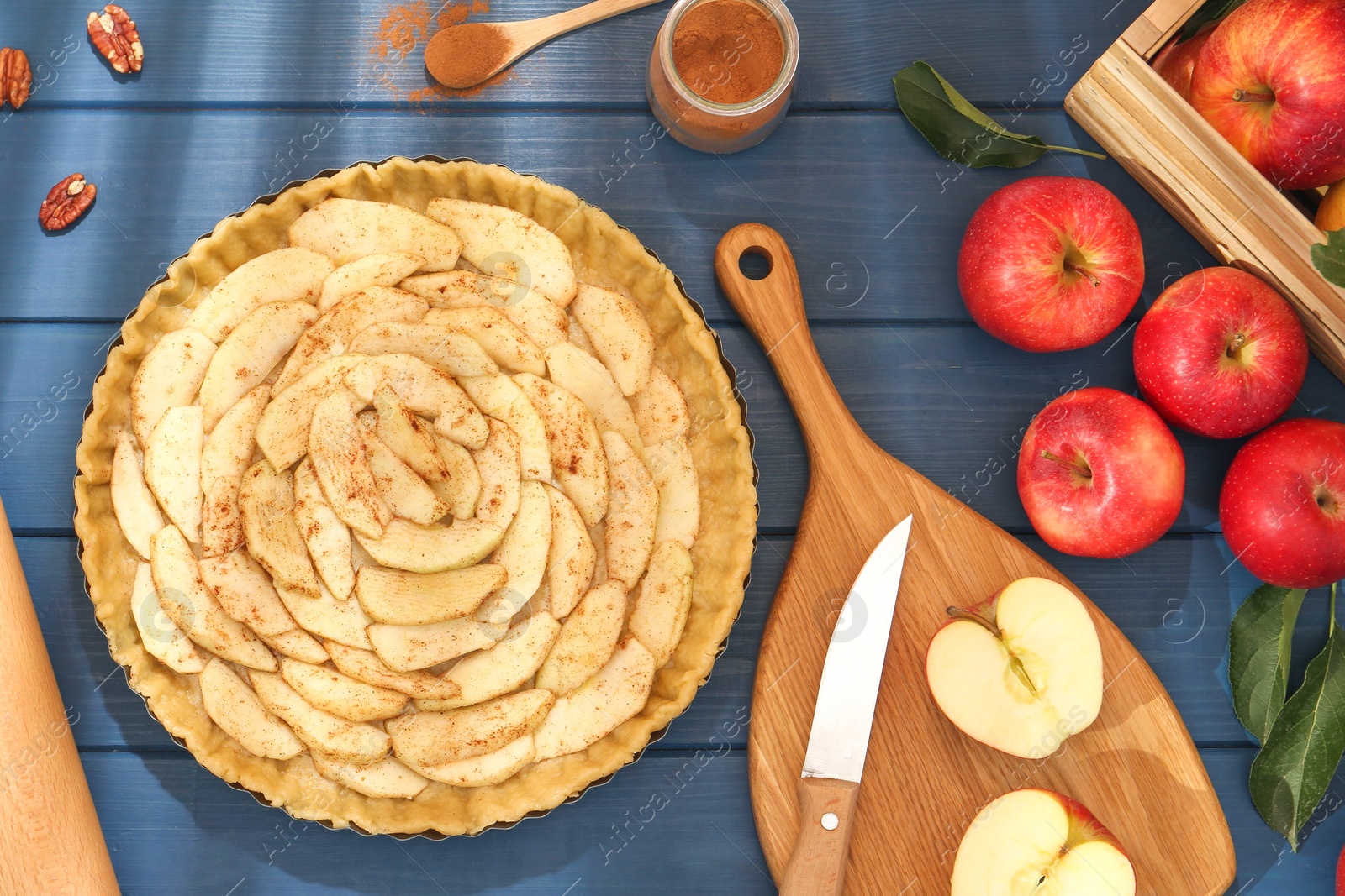 Photo of Uncooked homemade apple pie and ingredients on blue wooden table, flat lay