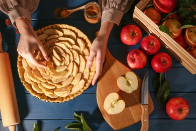 Photo of Woman making homemade apple pie and ingredients on blue wooden table, top view