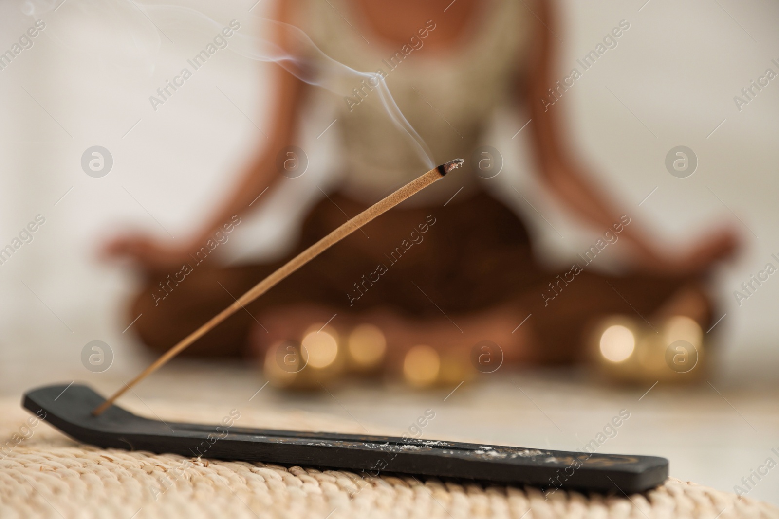 Photo of Incense stick smoldering in holder on wicker mat indoors, selective focus