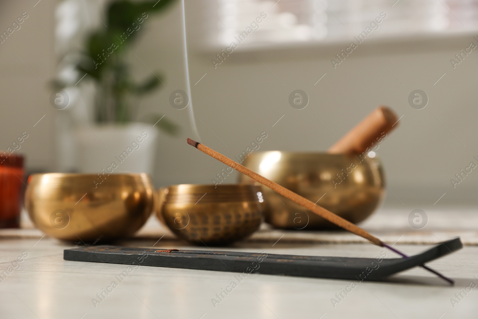 Photo of Incense stick smoldering in holder and tibetan singing bowls on floor, selective focus