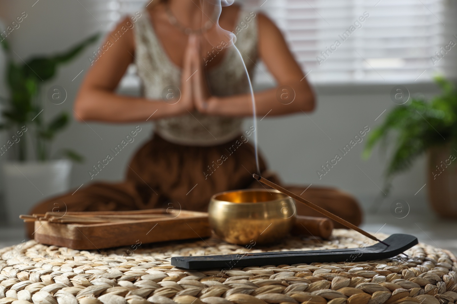 Photo of Young woman practicing yoga indoors, focus on smoldering incense stick and tibetan singing bowl